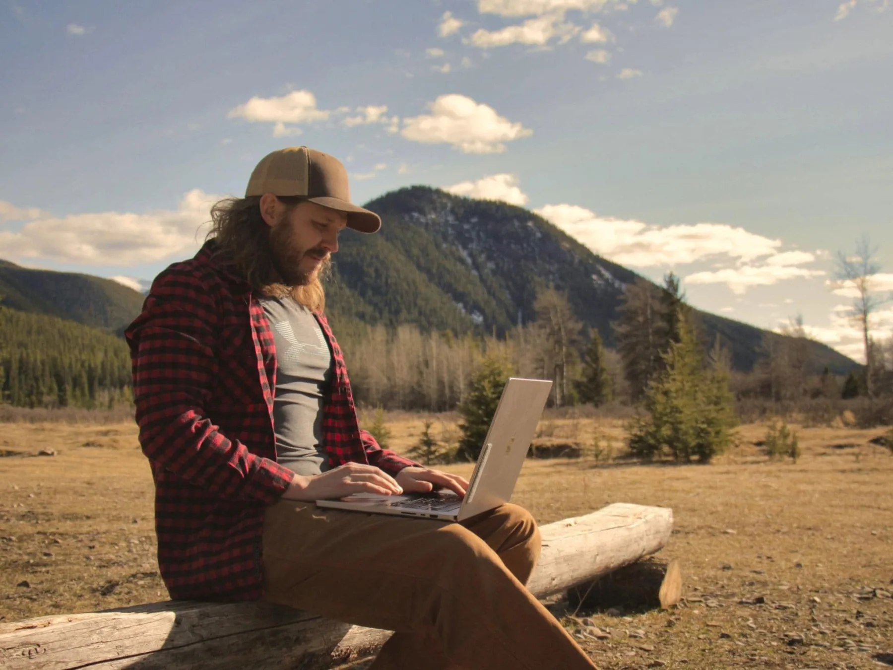 Brody Bestluck working on a laptop with the Alberta Rockies behind him